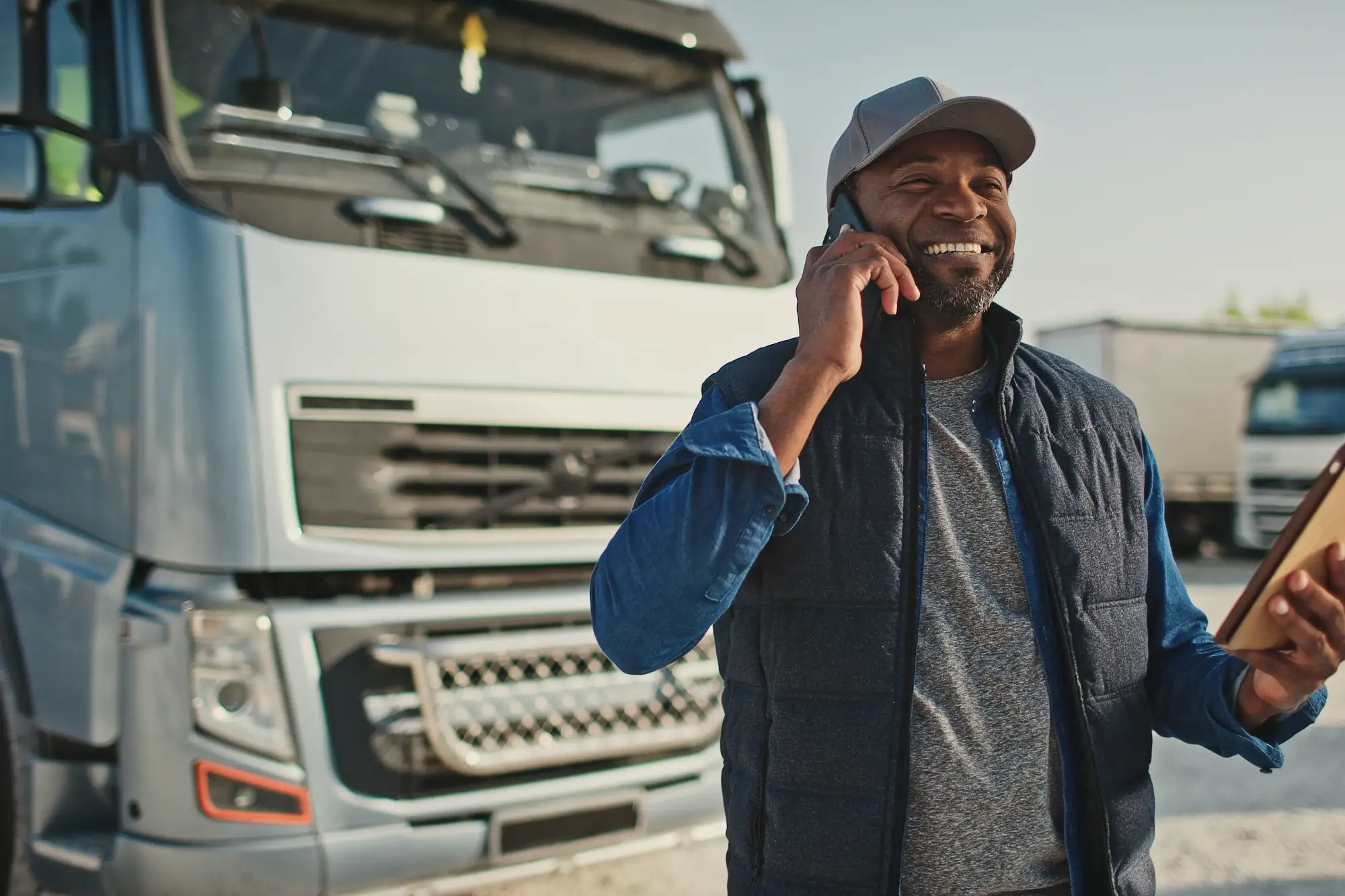 Smiling man holding phone to ear holding clipboard in front of a semi-truck.