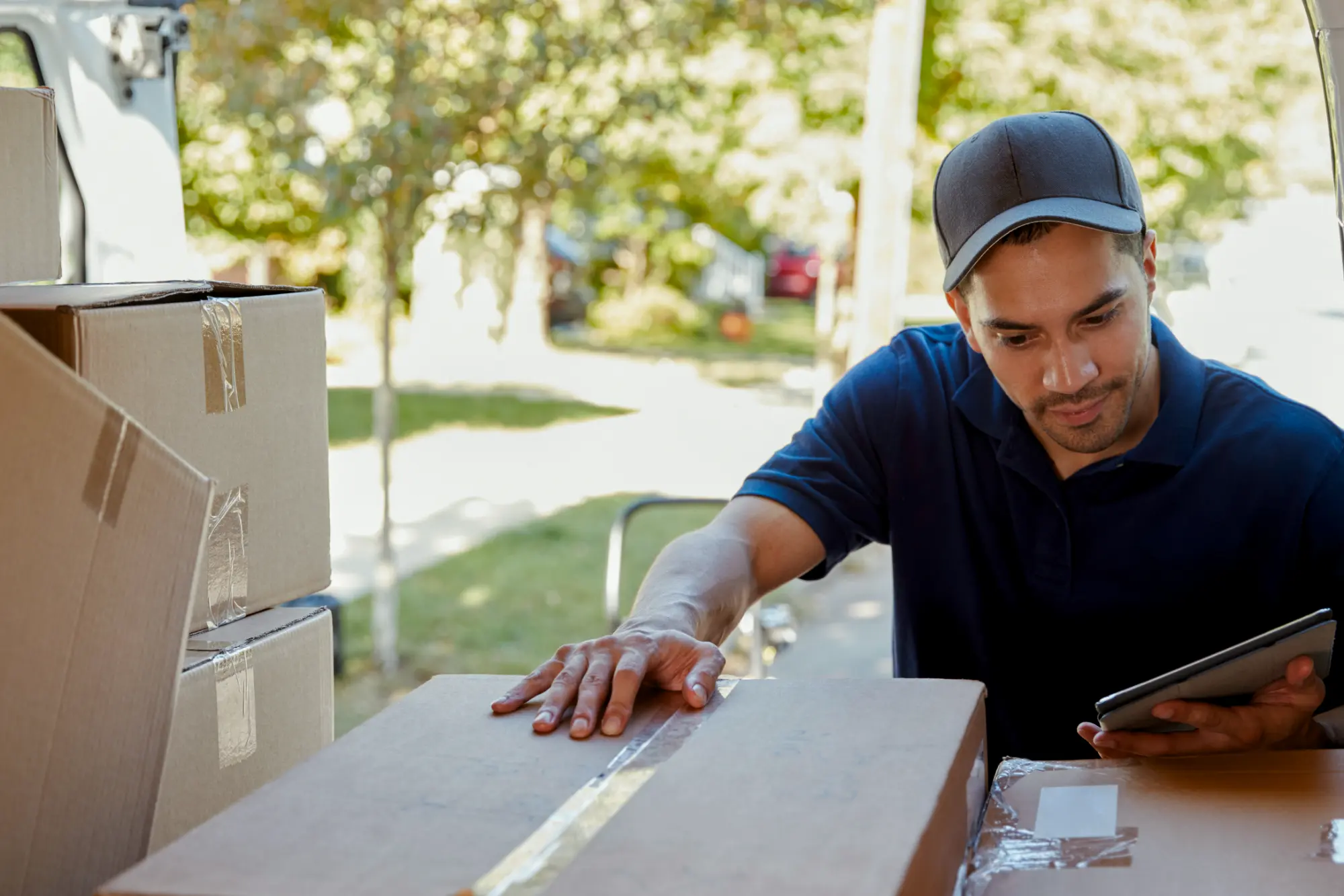 Delivery man with hat and tablet looking at boxes in back of van.