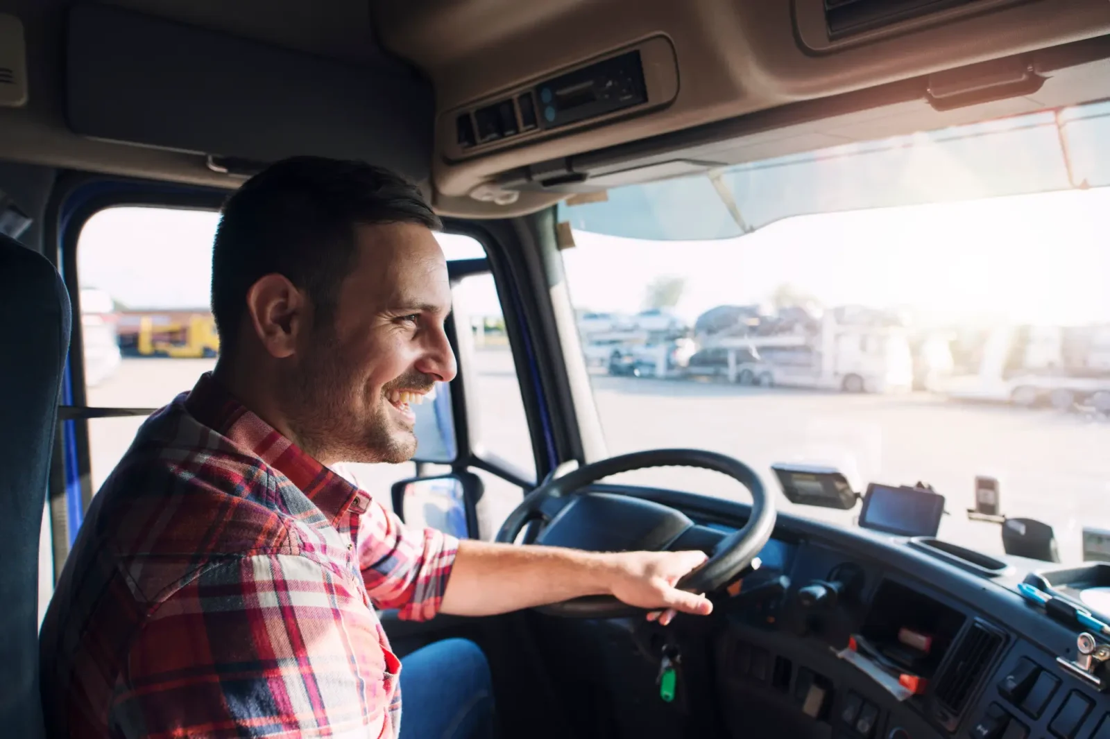 Smiling man in plaid shirt driving semi-truck.