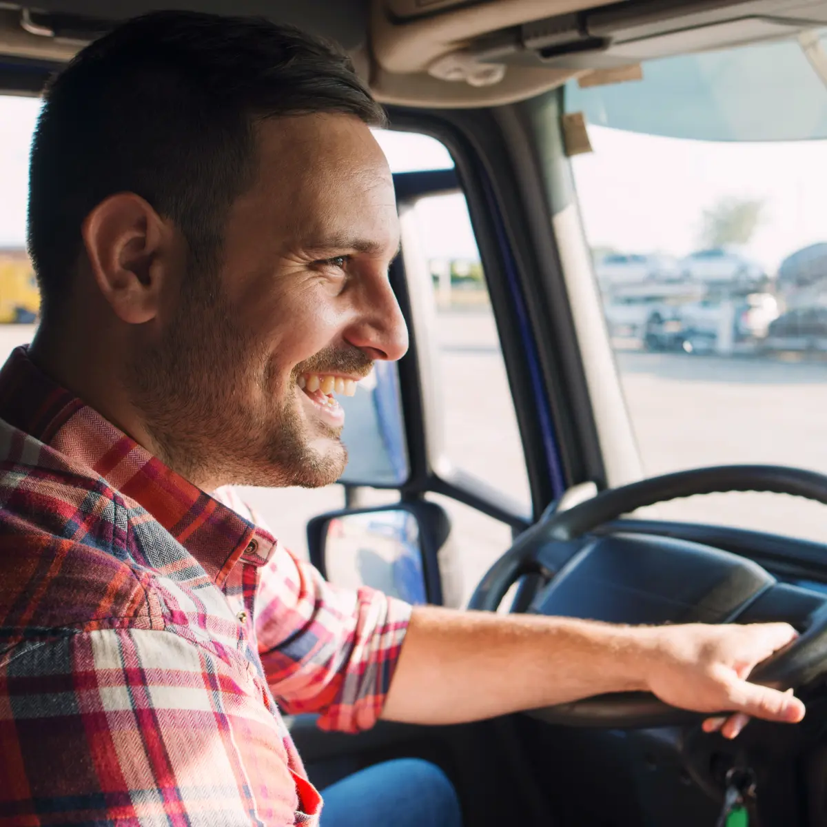Smiling man in plaid shirt driving semi-truck.