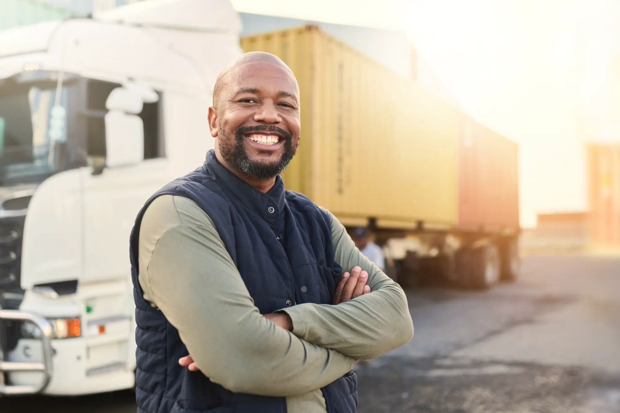 Smiling man with arms crossed standing in front of a semi-truck.