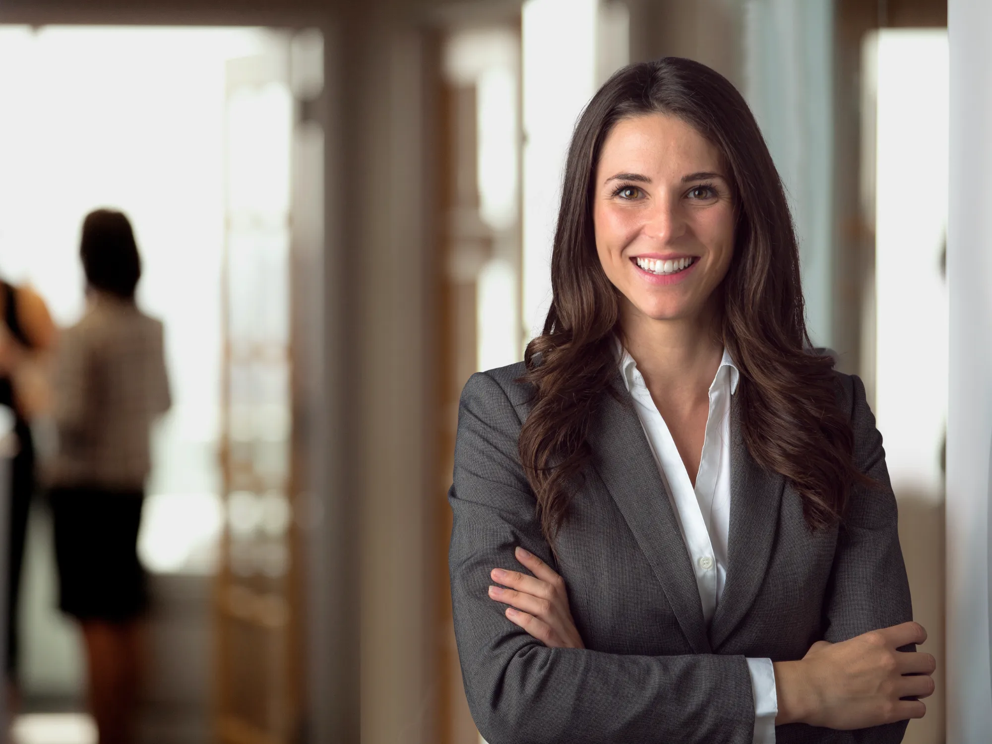 A young professional woman dressed in a suit with crossed arms smiling at the camera.