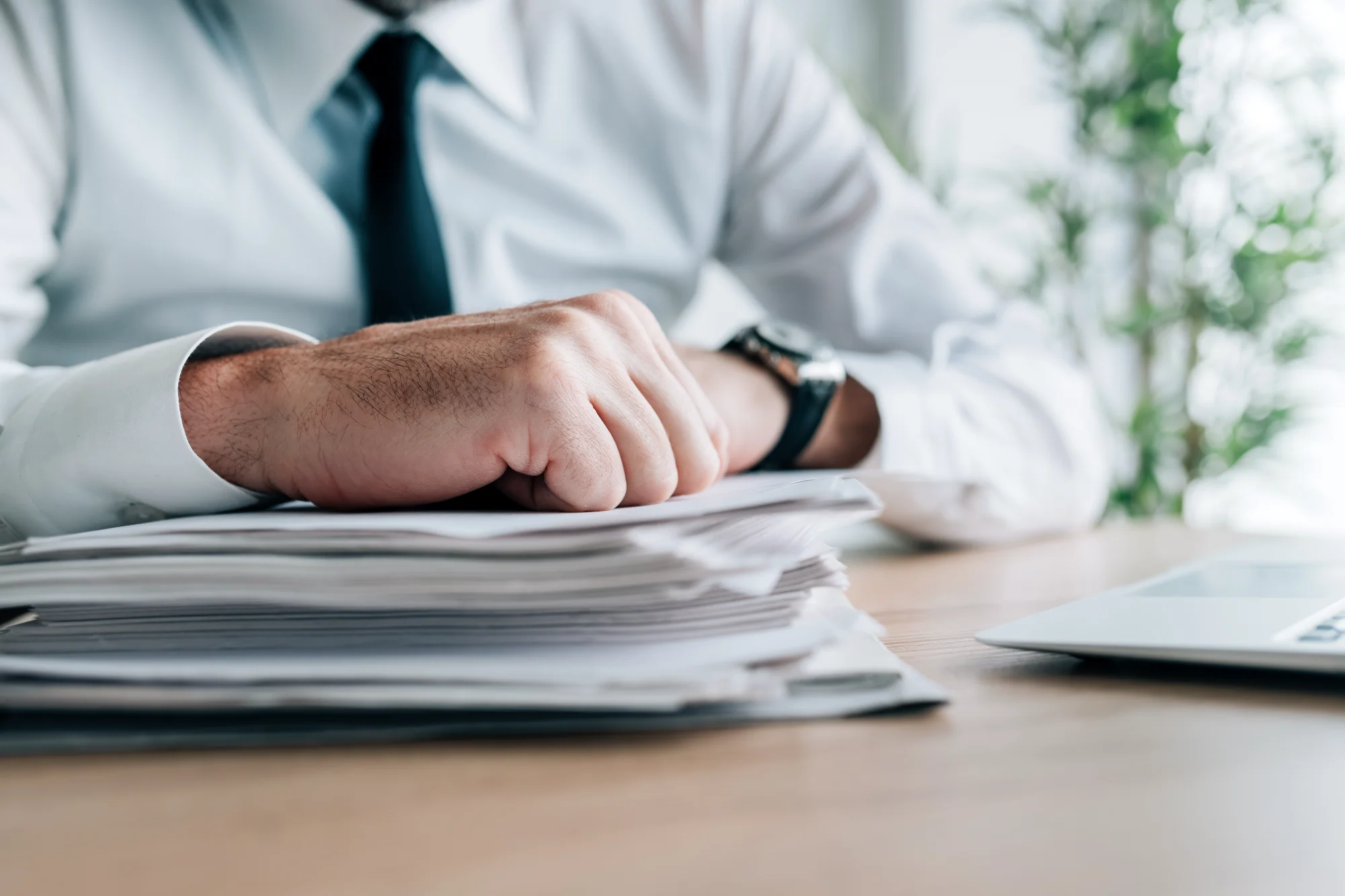 A professional in a white shirt and tie places a determined fist on a large stack of HR applications on a desk.